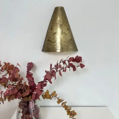 Handmade wall lamp in gold metal with a Moroccan pattern, hanging above a bookcase with a vase on it