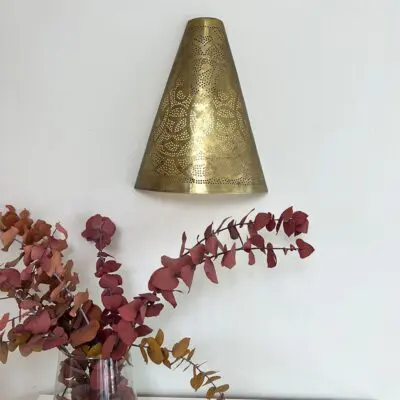 Handgemaakte wandlamp van goud metaal met een Marokkaans patroon, hangend aan een witte muur met daaronder bloemen