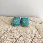 Marockanska handgjorda tofflor i turkos med vitt mönster ovanpå beni ouarain matta