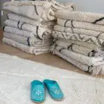 Marokkanske håndlavede slippers i turkis med hvidt mønster, oven på beni ouarain tæppe