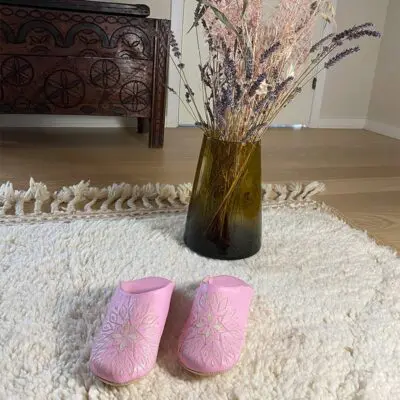 Moroccan handmade slippers in pink with white pattern on top of beni ouarain rug with vase behind