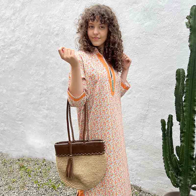 Model bærende taske i marokkansk håndvævet kjole i flerfarvet blomstermønster ved siden af kaktus