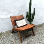 Håndlavet loungestol i valnøddetræ og sæde i flettet læder med pude ovenpå, stående ved siden af kaktus