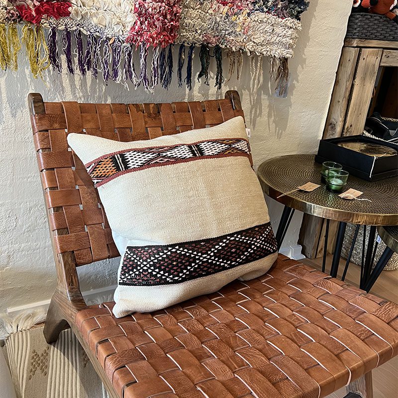 Håndvævet vintage kelim montagne pudebetræk i beige med marokkansk mønster i sort, rød og hvid stående på loungestol med bord ved siden af
