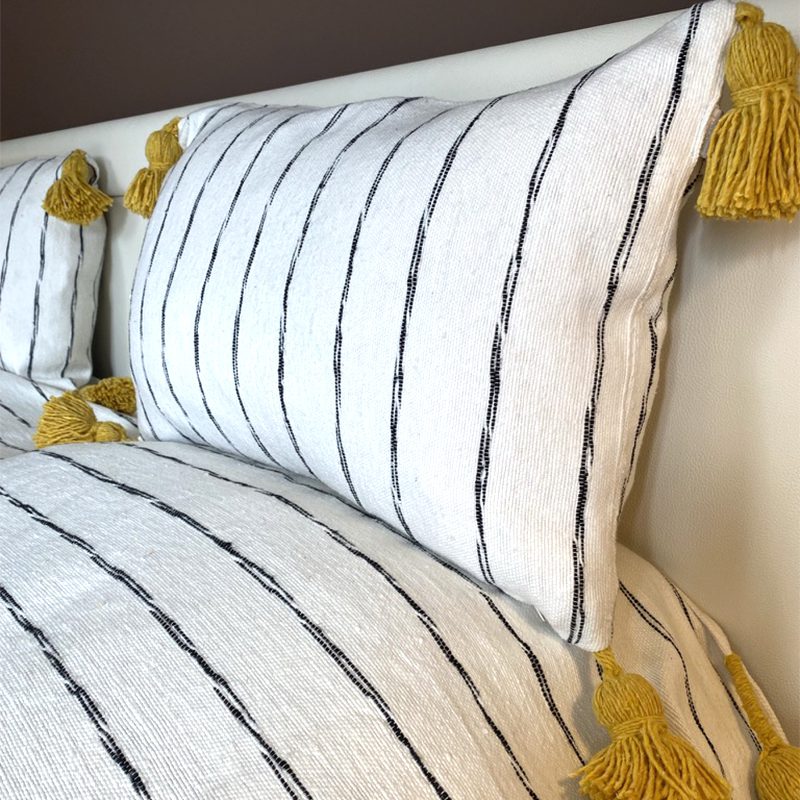 Hvidt marokkansk håndvævet sengetæppe med sorte striber og gule pomponer, med matchende puder