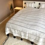 Hvidt marokkansk håndvævet sengetæppe med sorte striber og sorte pomponer på seng med matchende puder