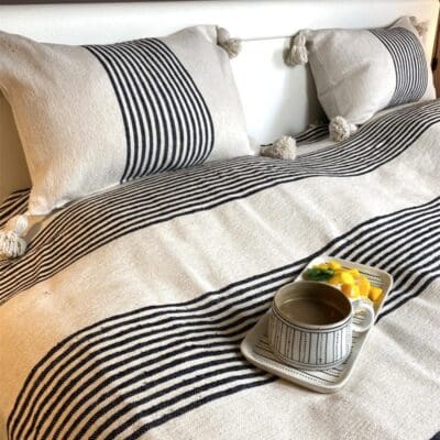 Hvidt marokkansk håndvævet sengetæppe med sorte striber og hvide pomponer, med morgenmadsfad