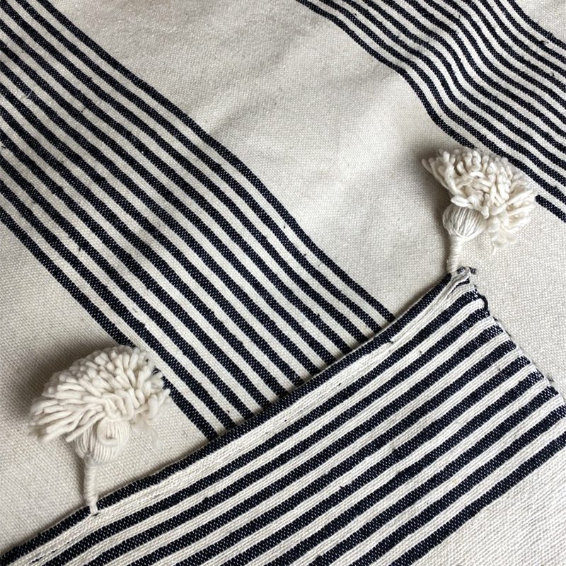 Hvidt marokkansk håndvævet sengetæppe med sorte striber og hvide pomponer