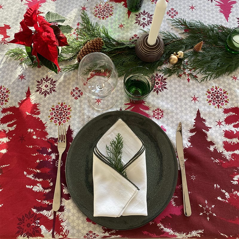 Marokkansk håndbroderet stofserviet med grøn kant på en tallerken på et opdækket bord med juledekorationer