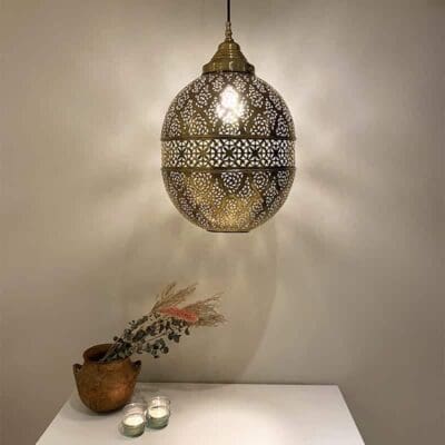 Stor håndlavet natlampe i guldmetal med marokkansk mønster, hængende over reol med dekorationer på