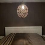 Stor håndlavet natlampe i guldmetal med marokkansk mønster, hængende over en seng