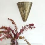 Håndlavet væglampe i guldmetal med marokkansk mønster, som der hænger over en vase med røde blomster i