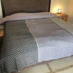 Marokkansk håndvævet sengetæppe med gråt firkantet mønster, liggende på en redt seng