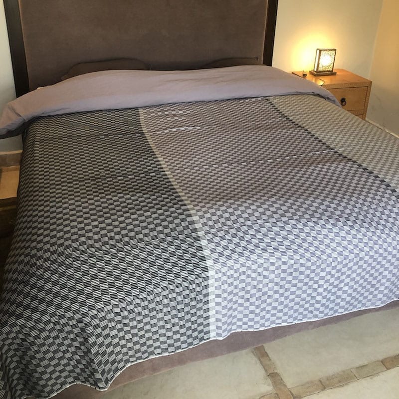 Marokkansk håndvævet sengetæppe med gråt firkantet mønster, liggende på en redt seng