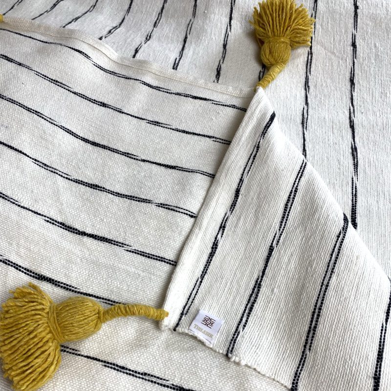 Hvidt marokkansk håndvævet sengetæppe med sorte striber og gule pomponer