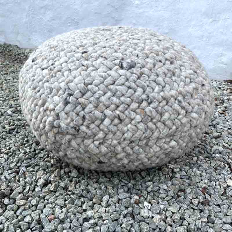 Rund marokkansk håndsyet uldpuf i beige og lysgrå, stående på sten udenfor