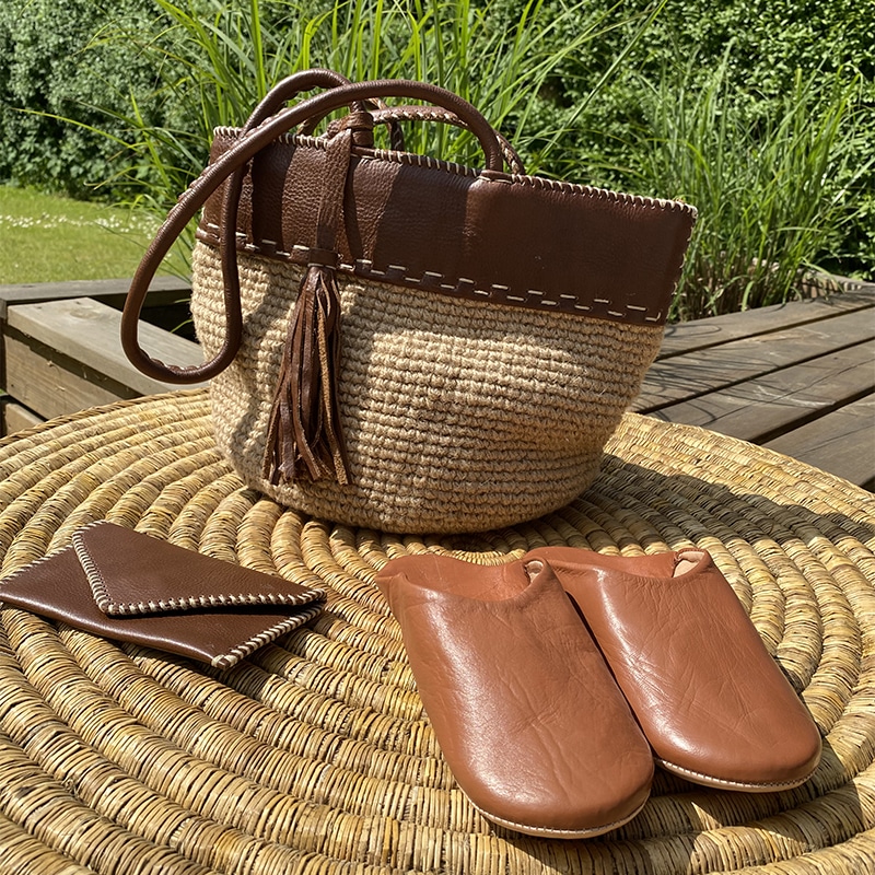 Marokkanske håndlavede slippers i brun, oven på flettet kurv med taske og pung ved siden af