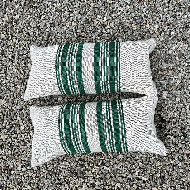 Aflange håndvævede puder med marokkansk mønster og grønne striber liggende på sten