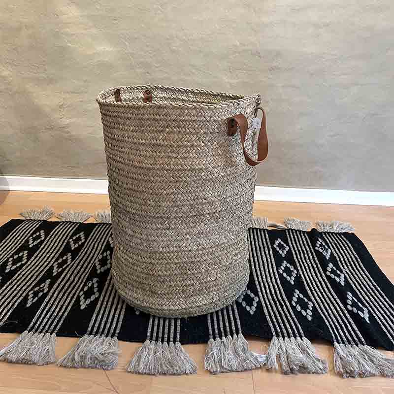 Marokkansk håndvævet kurv med læderhåndtag stående på tæppe