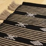 Håndvævet bomuldstæppe i sort med marokkansk stribe og prikmønster i brune og hvide nuancer med brune kvaster, tæt