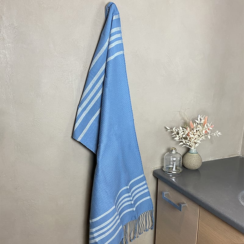 Marokkansk håndvævet hammam håndklæde i blå hængende på en krog ude på et badeværelse