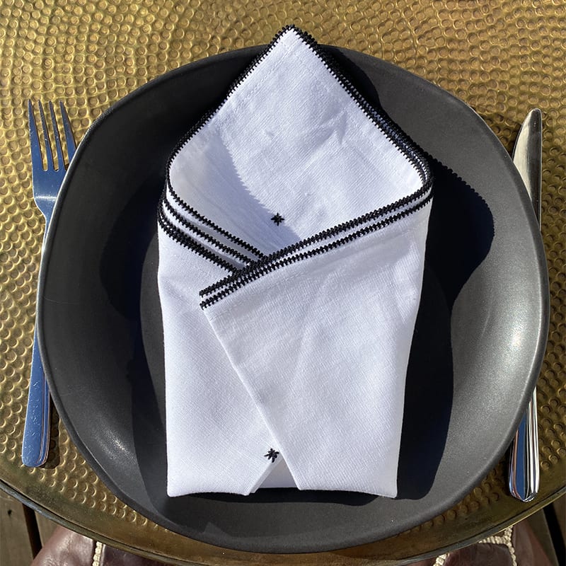 Hvid stofserviet med marokkansk håndbroderet mønster på en tallerken, med kniv og gaffel ved siden af