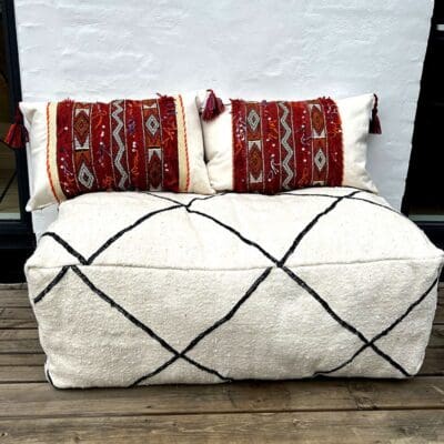 Handwoven vintage kilim boho cushion covers in red and beige with Moroccan pattern with tassels on the edges standing on a pouf