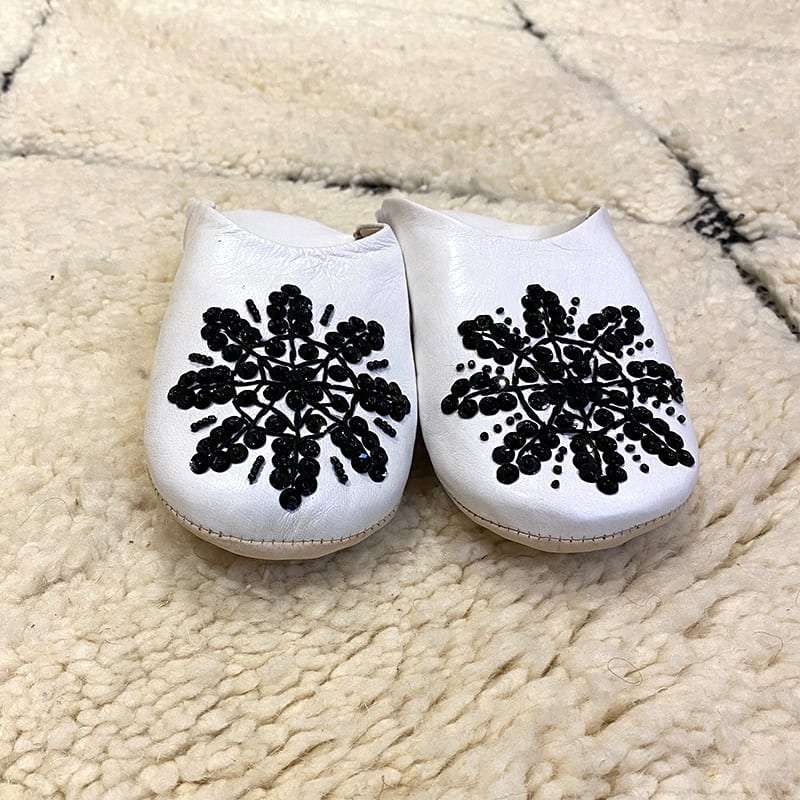 Marokkanske håndlavede slippers i hvid med sorte palietter, oven på Beni Ouarain tæppe