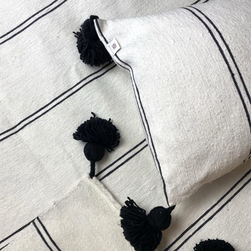 Hvidt marokkansk håndvævet sengetæppe med sorte striber og sorte pomponer, med matchende puder, tæt