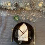 Marokkansk håndbroderet stofserviet med brun kant på en tallerken på et opdækket bord med juledekorationer