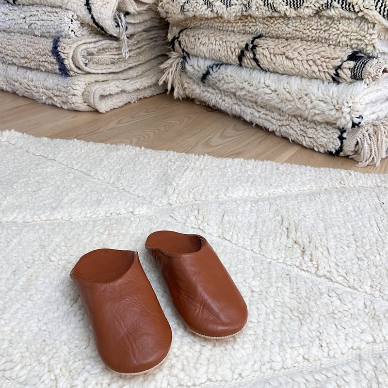 Marokkanske håndlavede slippers i brun, oven på beni ouarain tæppe