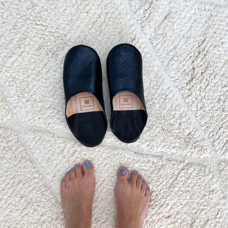 Marokkanske håndlavede slippers i sort med fodmodel ved siden af