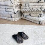 Marokkanske håndlavede slippers i sort med hvidt mønster oven på beni ouarain tæppe