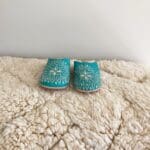 Marokkanske håndlavede slippers i turkis med hvidt mønster oven på beni ouarain tæppe