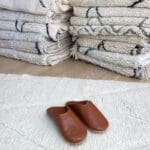 Marokkanske håndlavede slippers i lysebrun oven på beni ouarain tæppe
