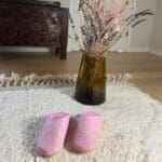Marokkanske håndlavede slippers i lyserød med hvidt mønster oven på beni ouarain tæppe med vase bagved