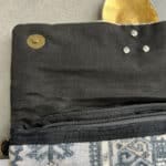 Handtas in grijstinten met koperen ketting en grote decoratieve knoop
