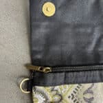 sac à main BIJOUX en tissu brillant dans les tons beige violet et vert gazon. Au centre se trouve un gros bouton en cuivre avec une pierre de couleur violette