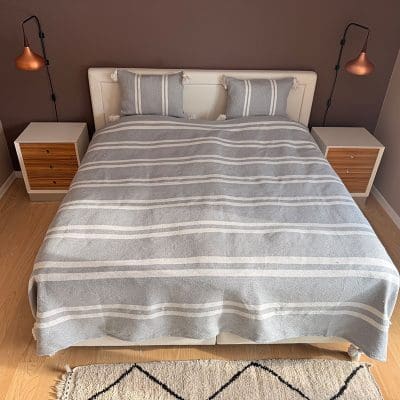 Smukt bomuldssengetæppe håndlavet i Marokko. Grå- og hvidstribet med pompommer i hvert hjørne.