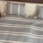 Smukt bomuldssengetæppe håndlavet i Marokko. Grå- og hvidstribet med pompommer i hvert hjørne.