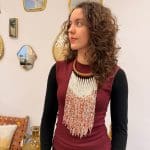 Pärlhalsband med halsring i ljusbrunt flätat läder och vita pärlor som dominerande färg. Orangea och gyllene pärlor blandas in och ger ett varmt och glödande uttryck, som påminner om saffran i snö.