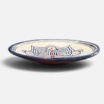 Assiette en céramique bleue ornée de motifs et de détails rouges et jaunes, fabriquée à la main au Maroc. Dimensions : 26 cm.