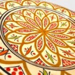 Assiette en céramique ocre ornée de détails rouges et verts, fabriquée à la main au Maroc. Dimensions : 26 cm.