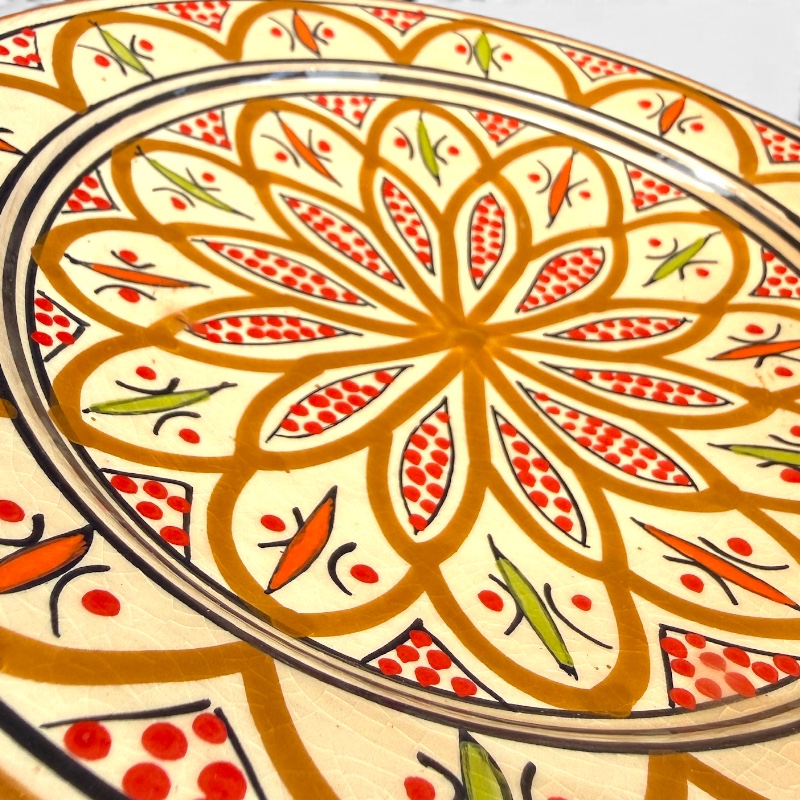 Assiette en céramique ocre ornée de détails rouges et verts, fabriquée à la main au Maroc. Dimensions : 26 cm.